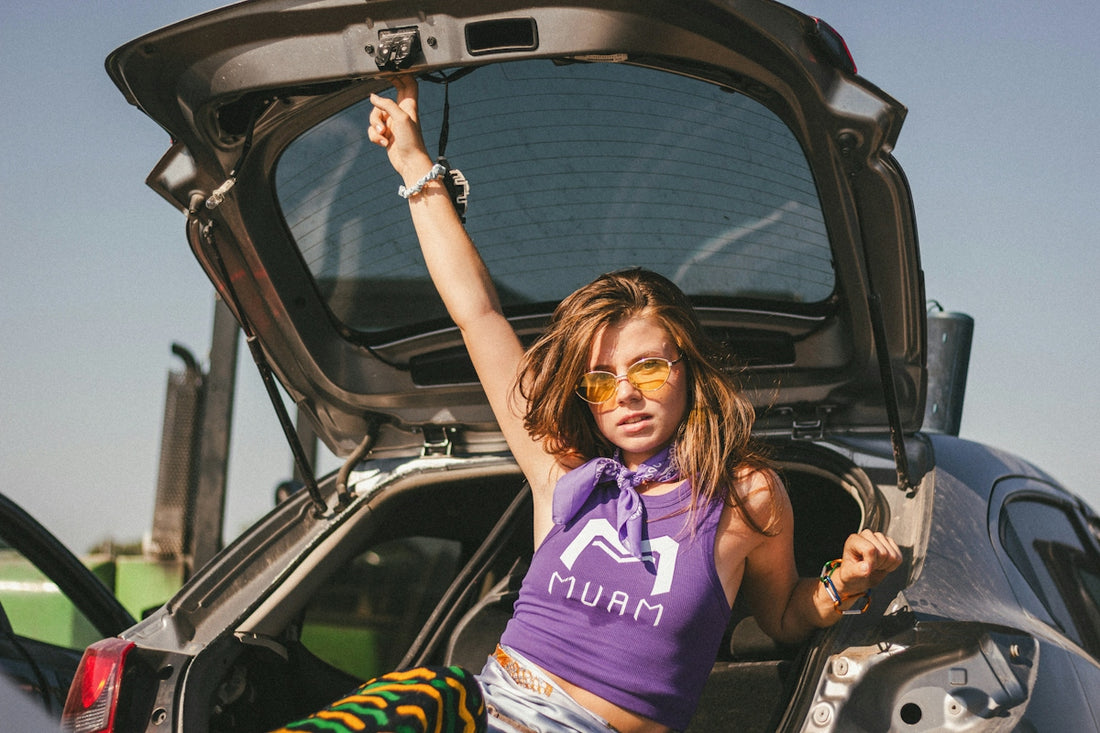 Stylish woman in sunglasses sitting in an open car trunk
